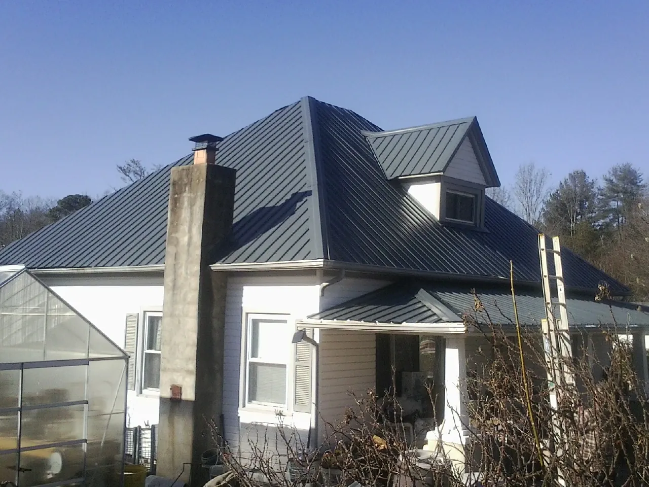 Dark blue standing seam metal roof on a white farmhouse with dormer — Slate & Tile Roof Repair by Roofing Brothers in North Haven