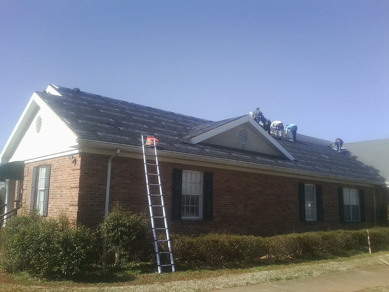 Crew tearing shingles off a brick ranch roof with a ladder set — Emergency Roof Repair work by our crew in North Haven