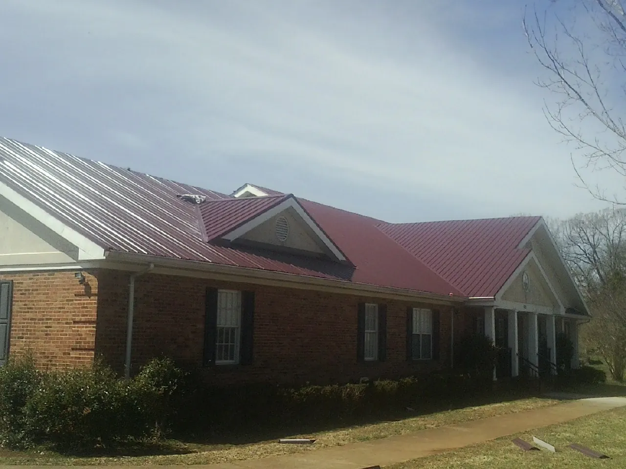 Red metal roof with gabled entries on a long brick building, from a Hail Damage Roof Repair job in North Haven