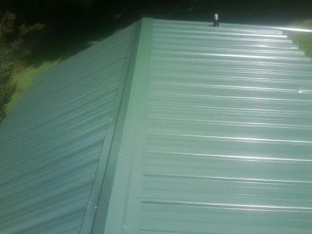 New green metal panels meeting at the ridge of a roof — Flat Roof Repair work by our crew in North Haven