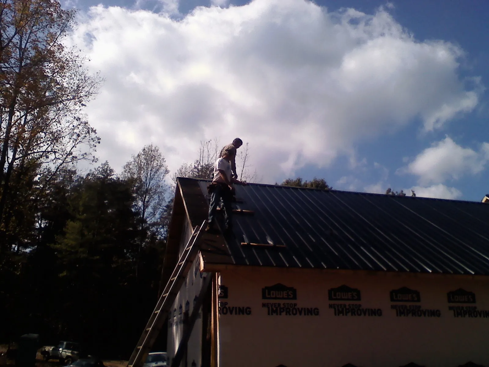 Roofer fastening dark metal panels high against a cloudy sky, from a Roof Inspection job in North Haven